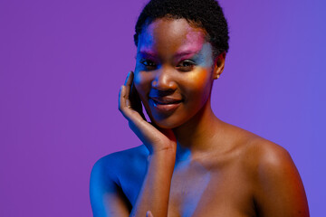 African american woman with short hair and colourful make up smiling with hand under chin