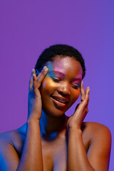 Smiling african american woman with short hair and colourful make up touching temples, copy space