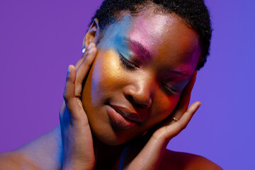 African american woman with short hair and colourful make up touching face with eyes closed