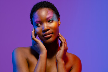 African american woman with short hair and colourful make up touching face and looking away