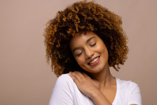 Smiling biracial woman with curly hair with hand on shoulder and closed eyes