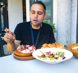 Young man eating vegetable salad and pulpo a la Gallega with potatoes. Galician octopus dishes. Famous dishes from Galicia, Spain.