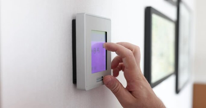 Room electronic thermometer shows temperature and humidity. Man regulates air temperature at home or office