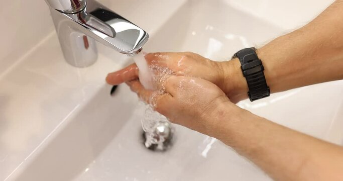 Closeup of cleaning hands with white soap bubbles at bathroom sink. Demonstration of hand washing to protect against viruses