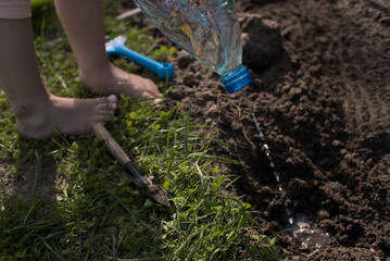 Little kid pouring water into a hole in ground from plastic bottle