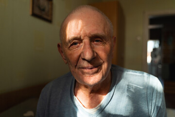 Close-up portrait of senior caucasian man at home in sunlight pocket. Retirement alone, loneliness of old man.