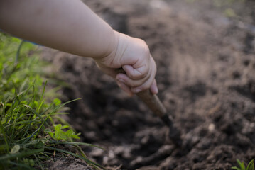 Little kids arm holding tiny shovel digging a hole in dark ground
