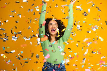 Studio Shot Of Excited Woman Celebrating Big Win Showered In Tinsel Confetti On Yellow Background