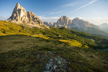 Sunrise at Passo Giau with sun shining from right side at meadow and peaks duraing summer morning in august at cloudless sky and warm light