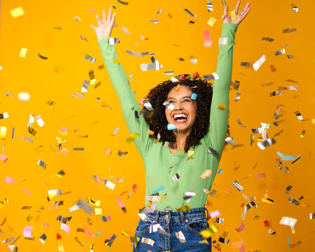Studio Shot Of Excited Woman Celebrating Big Win Showered In Tinsel Confetti On Yellow Background
