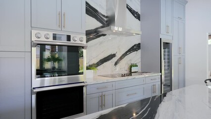 Luxurious bright matte kitchen with white cabinetry and built-in modern appliances from stainless steel. Glossy quartz splashback and island with black pattern