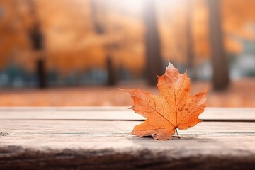 Naklejka na ściany i meble Autumn maple leaf on wooden table in front of blurred background.