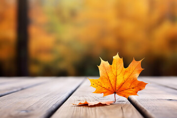 Naklejka na ściany i meble Autumn maple leaf on wooden table in front of blurred background.