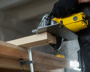 Master cuts the board with a circular saw in the workshop. Close-up of a carpenter's hands at work. 