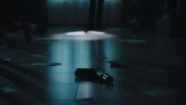 Closeup shot of the floor in the dark room. Gun, money, jewellery and traces of blood on it. Policeman in the background.