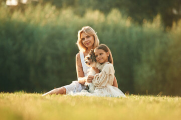 With cute dog. Mother with her daughter are on the field outdoors