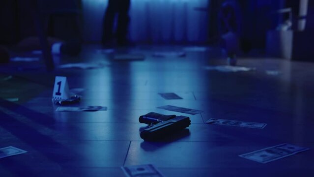 Closeup shot of the floor in the dark room. Handgun, money, jewellery and traces of blood on it. Policeman puts evidence numbers.