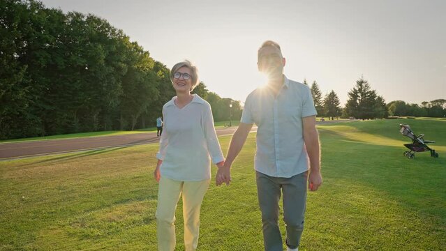 Older couple holding hands and walking on sunlit open area