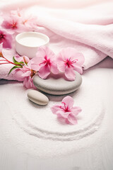 A spa setting with pink flowers, white towels and gray stones. The image is taken from a top-down perspective. A white textured surface with a zen-like circular pattern drawn in the sand.