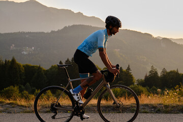 A fit male cyclist practicing on a gravel road at sunset. He is riding a gravel bike with a view of...