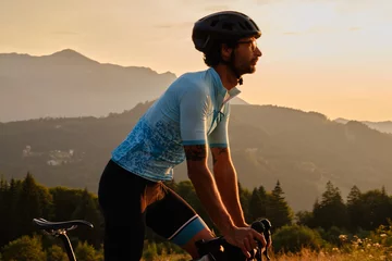 Foto op Canvas Man cyclist wearing blue cycling jersey. He is riding a gravel bike on a gravel road at sunset with a view of the mountains.Empty mountain road.Cycling gravel adventure in Romania.Bucegi Natural Park © Ketrin