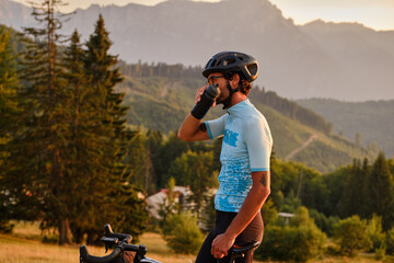 Man cyclist in mountain terrain quenches his thirst during intense training. Male cyclist in...