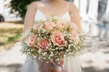 bride is holding a wedding bouquet.beauty of tea roses and gypsophila.Close-up of a bouquet of flowers.Wedding accessories.Details for marriage and married couple