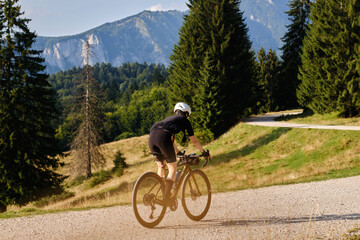 Female cyclist is riding on a gravel road with a mountain view. The athlete is wearing full cycling gear and training for a cycling competition. Cycling gravel adventure in Romania.Bucegi Natural Park