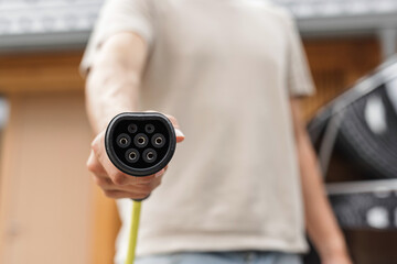 Young man plugging a charger in electric car at modern house home