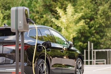 Electric car with plugged charger cable at an electric vehicle charging point in the parking lot in the city. Renewable energy concept. © 24K-Production