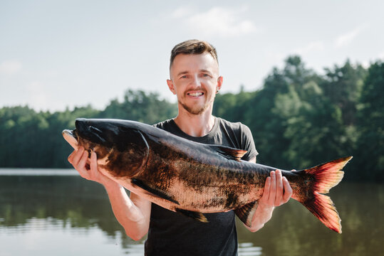 Fishing backgrounds. Happy fisherman hold big trophy fish near lake. Success pike fishing. Big fresh fish trophy in hands. Young man returning with a freshly caught fish. Article about fishing day.