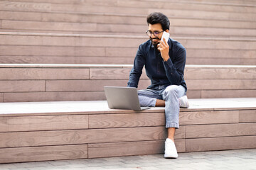 Indian freelancer young man talking on phone while using laptop
