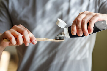 Applying toothpaste on a bamboo tooth brush. Hands squeezing tube with a toothpaste.