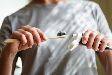 Applying toothpaste on a bamboo tooth brush. Hands squeezing tube with a toothpaste.
