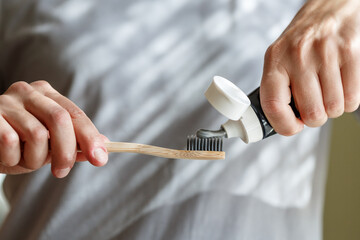 Applying toothpaste on a bamboo tooth brush. Hands squeezing tube with a toothpaste. - 644053141
