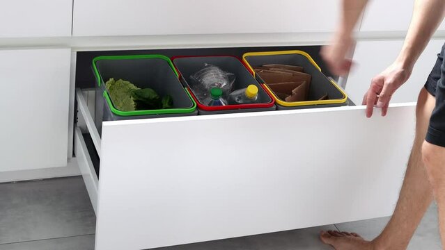 A young man sorts garbage in containers in the kitchen. Modern kitchen with a system for sorting waste. Waste Separation Concept. Zero waste. Eco-friendly. 4K footage