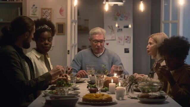 Multi-ethnic family of five multi-generational members talking to each other while enjoying food sitting at table