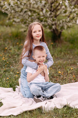 Portrait of a boy and a girl in the park. Brother hugging sister in the park against the background of green trees and apple flowers, friendship concept.