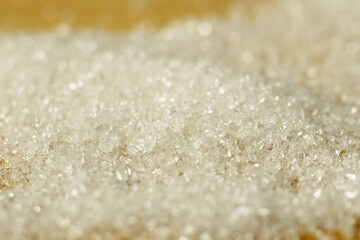 Macro spoon with sugar granules on a wooden table. Close-up of sugar crystals