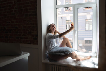 young beautiful woman talking on the phone sitting by the big window in the apartment