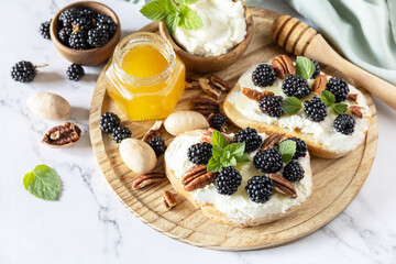 Keto diet sandwiches, snack. Sweet bruschetta with cheese and berries blackberry ricotta and honey on marble table. Healthy breakfast toasts.