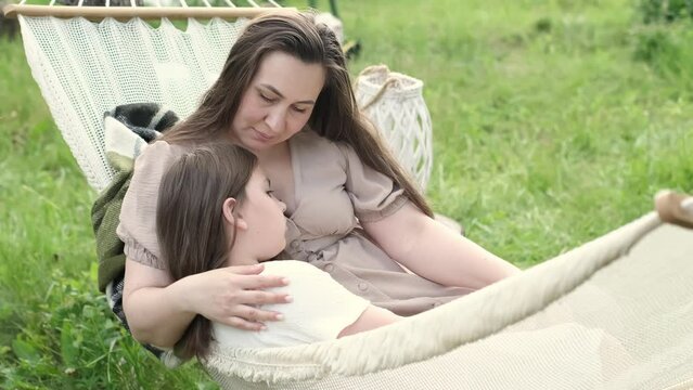 devoted mother and her young daughter share love and laughter, nestled in cozy hammock during a warm evening. This serene interaction exemplifies family bonds, outdoor relaxation