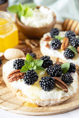 Keto diet sandwiches, snack. Sweet bruschetta with cheese and berries blackberry ricotta and honey on marble table. Healthy breakfast toasts.