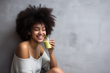 a smiling young woman drinking a smoothie while sitting against the wall