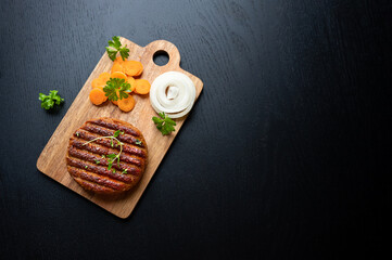 Fototapeta na wymiar Cutting board with grilled vegan plant-based meat carrots and onion on black background.