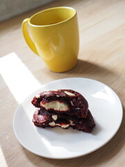 Red Velvet Cookies White chocolate on a wooden table, yellow coffee mug ,natural light