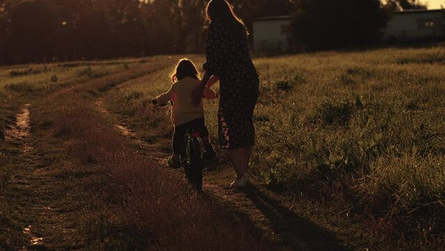 Games with children in the fresh air. mother teaches her child to ride a bicycle. mother with her son and a bicycle in the evening sunshine, in the field.
