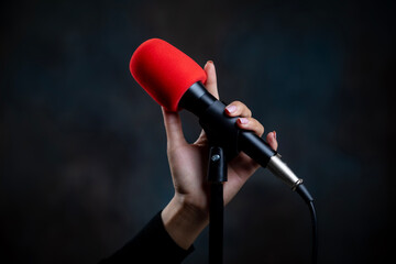 Woman's hand holding microphone on stand on black background. - obrazy, fototapety, plakaty