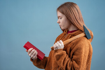 a young woman in a brown sweatshirt is reading a book and holding a hammer on her shoulder