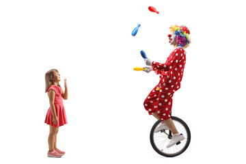 Full length profile shot of a surprised girl looking at a clown juggling and riding a unicycle